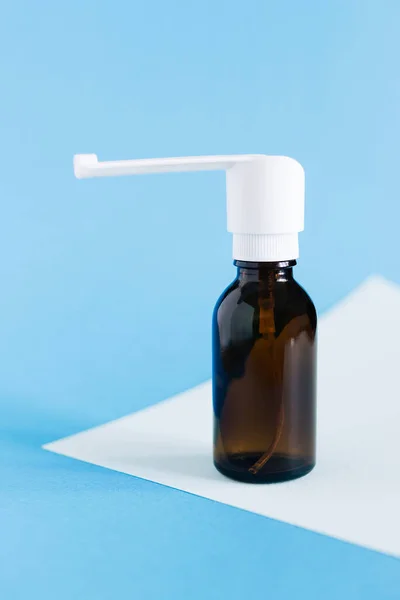 Health and pharmacy remedies for prevent and therapy disease and illness - glass Throat spray bottle mockup on blue wall, copy space.