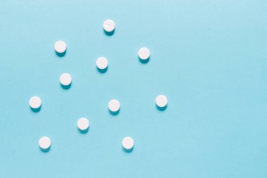 Mavi masaya saçılmış beyaz haplar. Reklam, web geçmişi ya da diğer fikirler için özel teklifler alın. Tıbbi, eczane ve sağlık hizmetleri konsepti. Uzayı kopyala Metin veya logo için boş yer