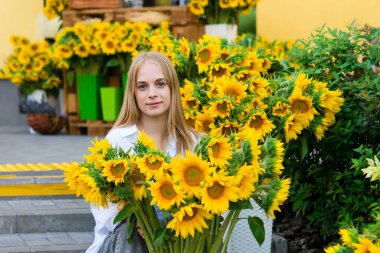 Girl teenager on the background of bright fresh sunflowers. flower shop making a bouquet of fresh flowers