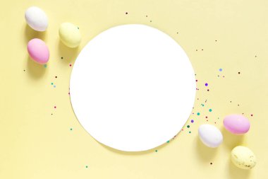 Paskalya dekoru konsepti. Pastel sarı arka planda beyaz daire, Paskalya yumurtası şeklinde çikolatalar, kopyalanmış uzay.