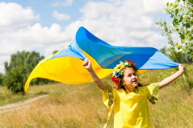 Ukraynalı çocuk Ukrayna bayrağı taşıyan, nakış işlenmiş ulusal kıyafetler ve çiçek çelengi giyiyor. Ukrayna 'nın Bağımsızlığı, Bayrak Günü, Anayasa Günü.
