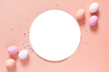 Mutlu Paskalya dekorları. Boş tebrik kartı, davetiye maketi. Pastel pembe arka planda beyaz daire, Paskalya yumurtası şeklinde çikolatalar. Kopyalama alanı, düz yatış, üst görünüm. 