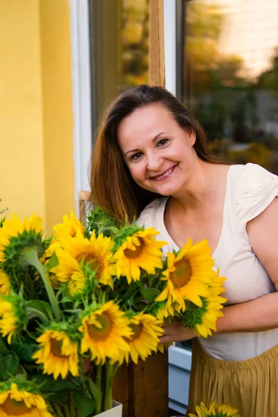 stock image Elegant adult woman with a bouquet of sunflowers flowers near a cafe - a flower shop.