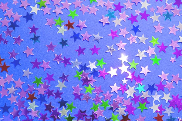 Multi-colored shining stars close-up. Festive holiday background. Stars on a blue paper background.