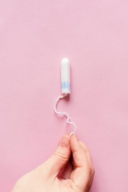 Pembe arka planda kadın hijyenik tamponu. Tamponlu bir kadın eli. Kritik günlerde hijyen bakımı, kadın sağlığıyla ilgilenmek. Aylık koruma. çoklu uzay. Adet döngüsü.