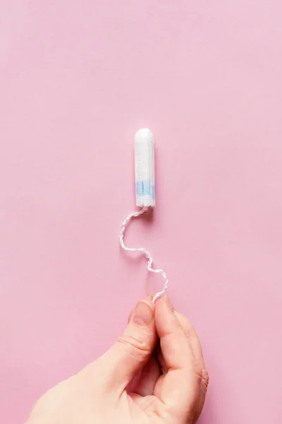 Feminine sanitary tampon on pink background. Woman\'s hand with a tampon. Hygiene care during critical days, caring for women\'s health. Monthly protection. copyspace. menstrual cycle.