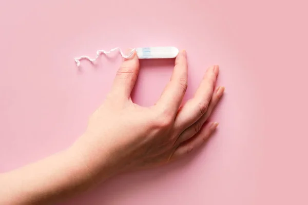 Feminine sanitary tampon on pink background. Woman's hand with a tampon. Hygiene care during critical days, caring for women's health. Monthly protection. copyspace. menstrual cycle.
