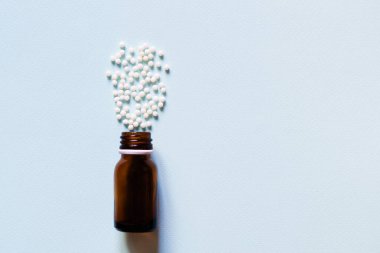 Homeopatik haplar ve mavi arka planda kahverengi şişe maketi. Homeopati alternatif tıp konsepti. Boşluğu kopyala.