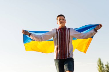 Ukraynalı çocuk Ukrayna bayrağı taşıyan, nakış işlemeli ve çiçek çelenkli ulusal kıyafetler giyiyor. Ukrayna 'nın Bağımsızlığı, Bayrak Günü, Anayasa Günü.