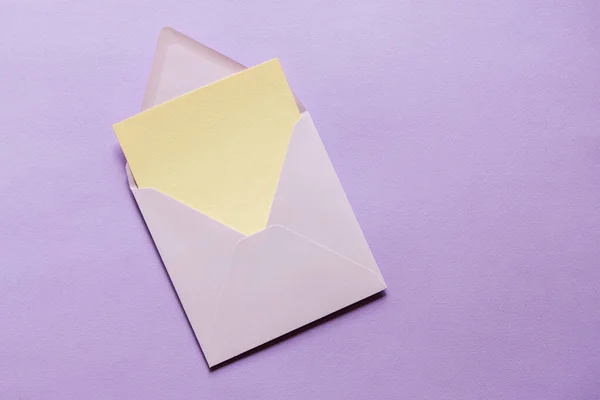 Blank greeting card mock up. Beige empty sheet of paper mockup in an violet envelope on violet paper background. flat lay. Wedding, business, birthday still life scene.