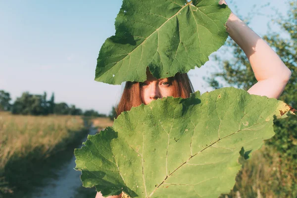 女性は2つの大きな緑の葉の後ろから外を見る 目を強調する — ストック写真