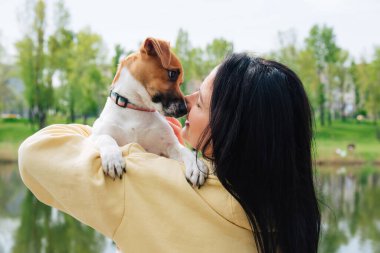 Kadın ve köpeğin yakın plan portreleri. Kadın köpeği kollarında tutuyor, sarılıyor. Güzel renkli yaz doğal manzarası