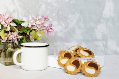 Açık gri masada siyah ve beyaz kurabiye (yin ve yang kavramı) ile beyaz metal fincanda sade kahve. Taze yaz çiçekleri. Çiçekli ev dekorasyonu.