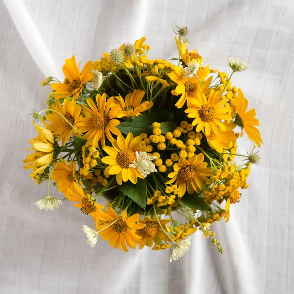 Bright yellow flowers in a round vase on a table with a white tablecloth. Happy mother's day, women's day or birthday pastel colors background. Floral minimalism greeting card.