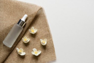 Makyaj ürünleri. Cilt bakımı için, güzellik ürünleri için, kozmetik ürünler için buzlu cam kap. Serum şişesi ve düşürücü. Moda ve güzellik blog konsepti. Kaba tuval ve yasemin çiçekleri.