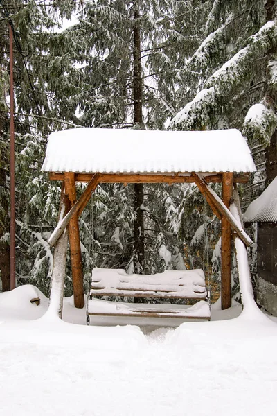 雪に覆われた木製のベンチ 冬にスイングします 雪の中で居心地の良いスイングとクリスマスツリーと冬の風景 — ストック写真