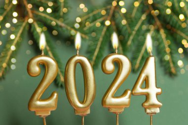 Yeni yılın kutlu olsun 2024 altın rakamıyla yeşil arka plan. Noel ağacı dalları ve altın dekoratif mumlarla süslenmiş Noel kartı afişi. Model, kartpostal..