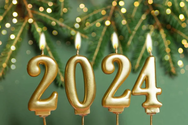 Happy new year 2024 green background with gold number. Christmas card banner with Christmas tree branches and golden decorative candles. Mockup, postcard.