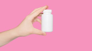 Elinde pembe arka planda izole edilmiş boş beyaz ilaç şişesi olan bir el. Uzayı kopyala Haplarla dolu bir şişe. Model.