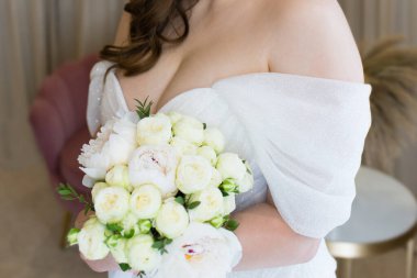 Gelin elinde bir buket beyaz çiçek, düğün buketi tutuyor. Gelin içeri gelsin. Koyu yaka.