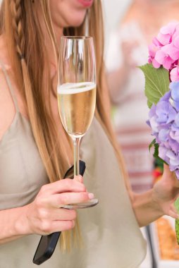 Elinde akıllı bir telefon ve elinde çiçeklerle elinde bir bardak şampanyayla mutlu bir kadın.