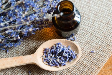 Aromaterapi için bir şişe bitkisel yağ ve tekstil arka planında lavanta çiçekleri. Alternatif tıp ya da parfüm. Tahta kaşıkta kurumuş lavanta çiçekleri..
