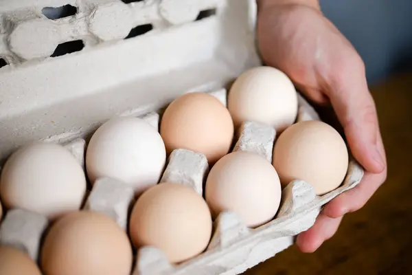 Male hands holding a cardboard egg box full of chicken eggs in the kitchen on table background
