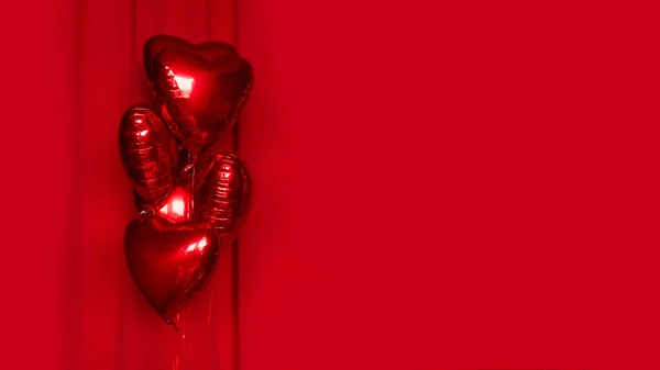 Red metallic helium balloons in the shape of a heart on a red fabric background. Foil balloons. Minimal love concept. Decoration for Valentine\'s Day or wedding party. Copy space, empty mockup, border