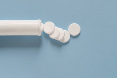 Mavi masadaki beyaz plastik bir konteynırın yanına yayılmış beyaz yuvarlak haplar. Özel teklifler için reklam yapın, internet geçmişi. Metin veya logo için boş kopyalama alanı