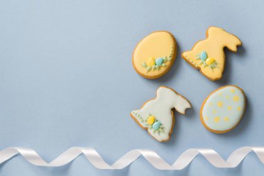 Paskalya 'da ev yapımı zencefilli çörek ya da kremalı kurabiye, tavşan ve yumurta desenli. Beyaz kurdeleli dekor. Mavi arkaplan, üst görünüm, kopyalama alanı