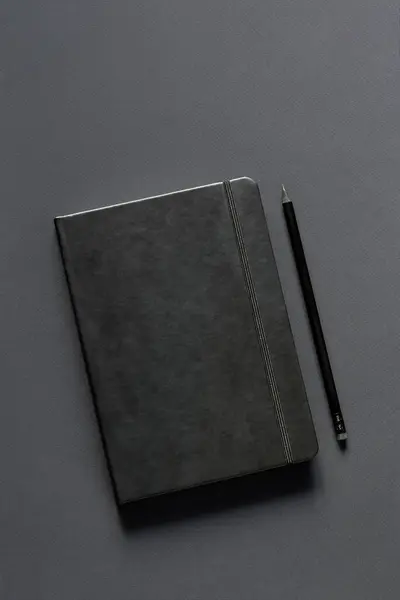 Blank black notepad and black pencil on a dark background. Monochrome photo. Business concept. Copy space for your text.