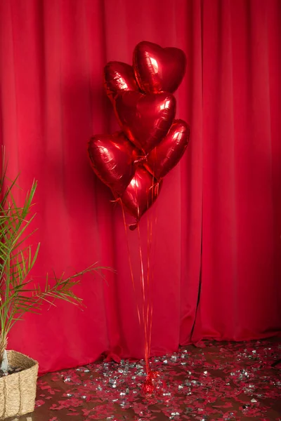 Red metallic helium balloons in the shape of a heart on a red fabric background. Foil balloons. Minimal love concept. Decoration for Valentine\'s Day or wedding party.