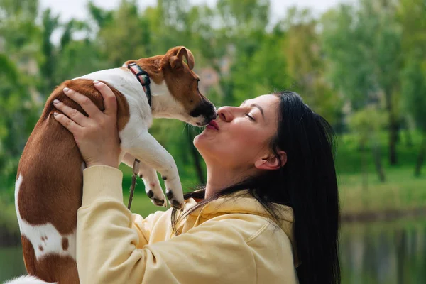 Woman and a dog close-up portraits. Woman holds a dog in her arms, hugs. Dog licks and kisses the owner. Jack russell terrier dog. Beautiful colorful summer natural landscape