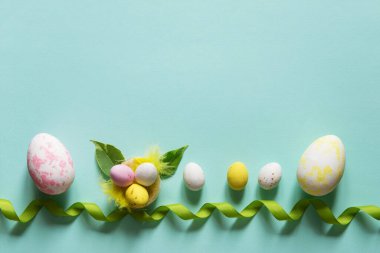 Paskalya yumurtası, yuva ve dekoratif kurdeleli Paskalya konsepti. Kopyalama alanı olan hassas pastel mavi arkaplan. Düz yatıyordu
