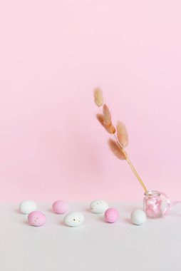 Pastel arka planda küçük benekli beyaz ve pembe çikolatalı yumurtalar, kuru renklerden bir buket. Metin için yeri olan Paskalya kartı.