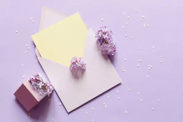 Lilac flowers, envelope and gift box over purple paper background. Flat lay, top view. Lovers or Women\'s day. Minimal floral frame made of flowers. Blank greeting card mockup.