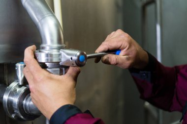 Tamircinin elleri manivelada. Fabrikada çalışan bir işçi. İşçi eli fabrikadaki bir makinenin kolunu çekiyor.