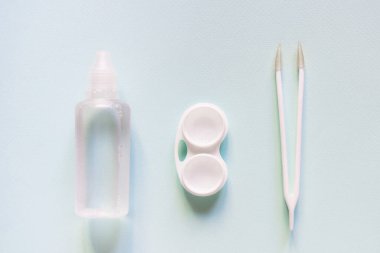 Contact lenses set with saline in bottle, tweezers, plastic case with solution on blue background with copy space