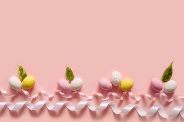 Renkli Paskalya şekerli yumurta ve pembe arka planda kurdele. Fotokopi alanına sahip en az biçimlendirilmiş Paskalya pankartı