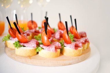 Kiraz domatesli kanepeler, salam, şifalı otlar ve ekmek ahşap bir tabakta. Kapat.