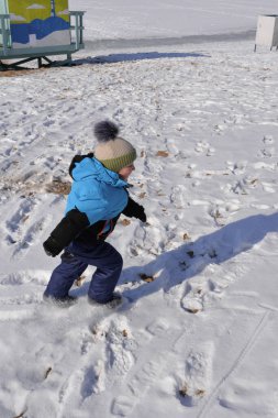 Küçük çocuk kışın koşuyor ve karla oynuyor.