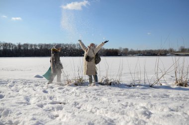 İki kız arkadaş kar atıyor, kış parkında karlı manzaralara karşı kartopu oynuyorlar.