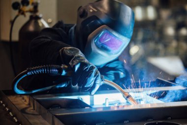Koruyucu maske takan fabrika işçisi demir parçaları kaynıyor..