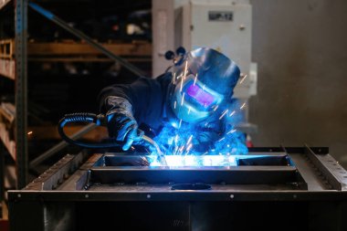 Koruyucu maske takan fabrika işçisi demir parçaları kaynıyor..