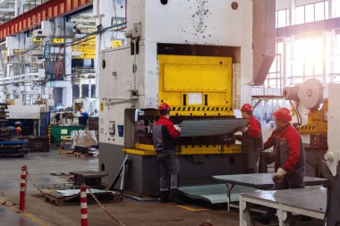CNC hidrolik basınç freninde metal levha ile çalışan teknisyenler.