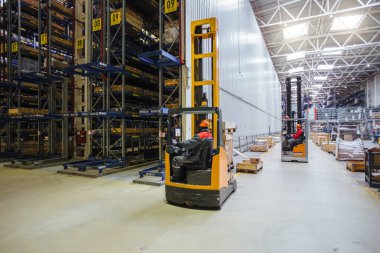 Modern deponun içinde rafları ve kutuları olan forklift yükleyicisi..
