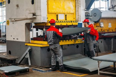 CNC hidrolik basınç freninde metal levha ile çalışan teknisyenler.