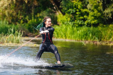 Dalgıç kıyafetli bir kız nehirde bir wakeboard 'un üzerinde duruyor..