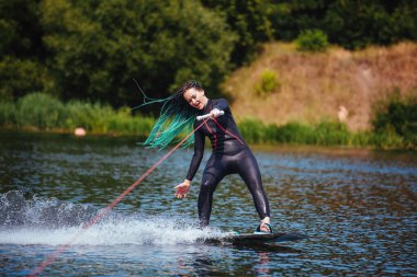 Dalgıç kıyafetli bir kız nehirde bir wakeboard 'un üzerinde duruyor..