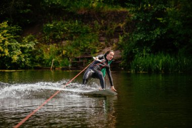 Dalgıç kıyafetli bir kız nehirde bir wakeboard 'un üzerinde duruyor..
